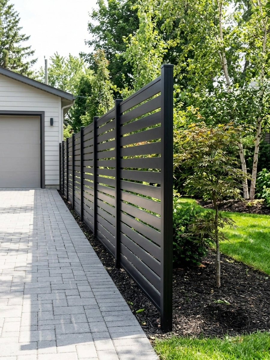 Black aluminum open slat fence installed along a paved driveway and landscaped yard