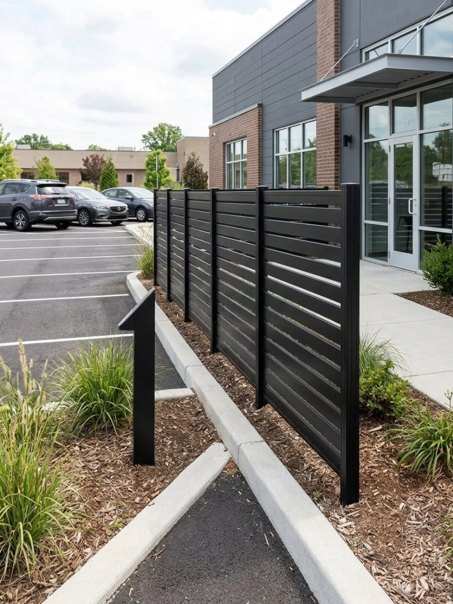 Black aluminum slat fence panels installed beside a commercial building entrance and parking lot